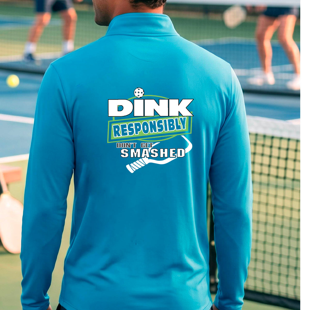 A man viewed from behind wearing a bright blue long-sleeve athletic quarter-zip jacket with a large back graphic that reads 'DINK RESPONSIBLY DON'T LET SMASHED' with a white pickleball graphic on the design. 