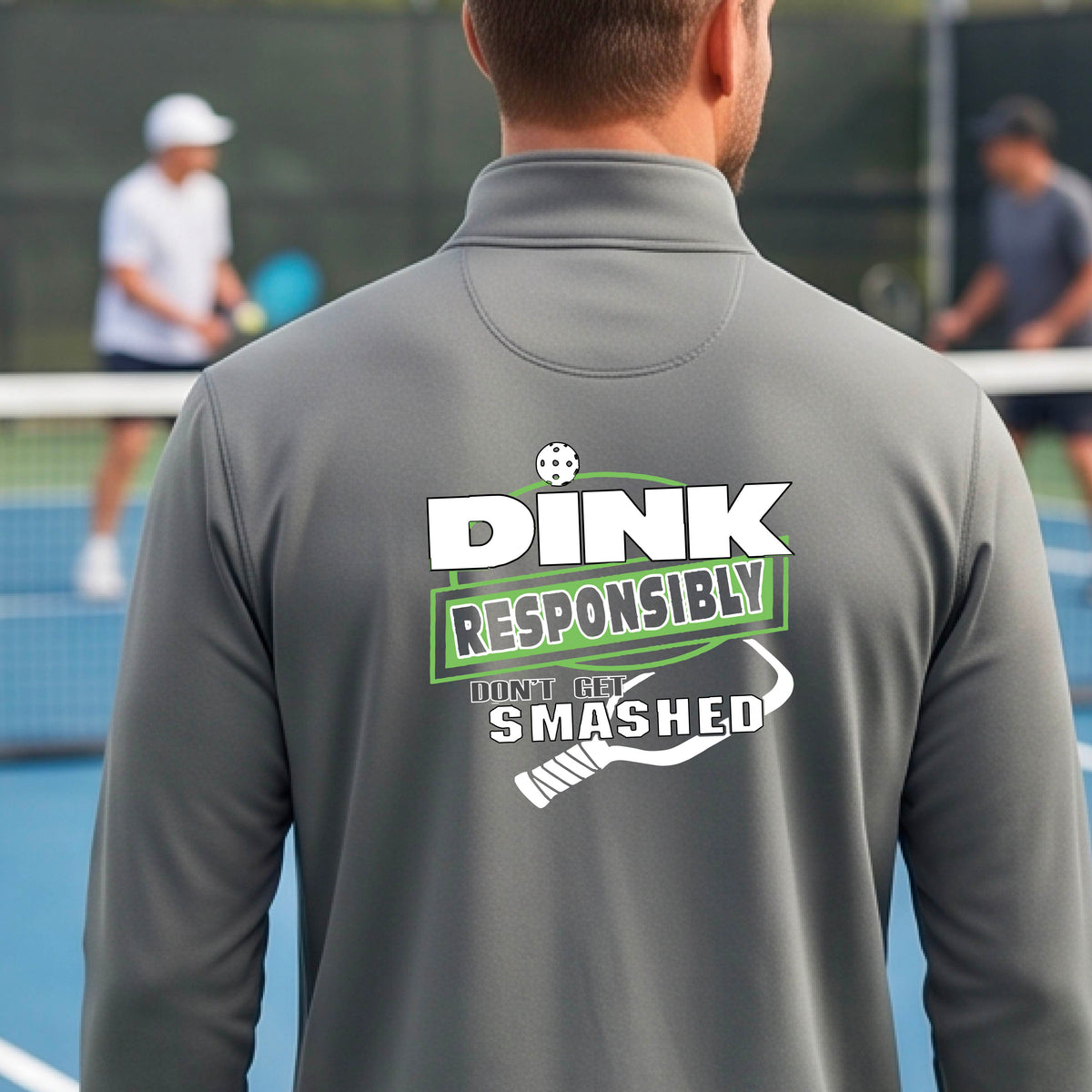 A man viewed from behind wearing a gray long-sleeve athletic quarter-zip jacket with a large back graphic that reads 'DINK RESPONSIBLY DON'T LET SMASHED' with a white pickleball graphic on the design. 