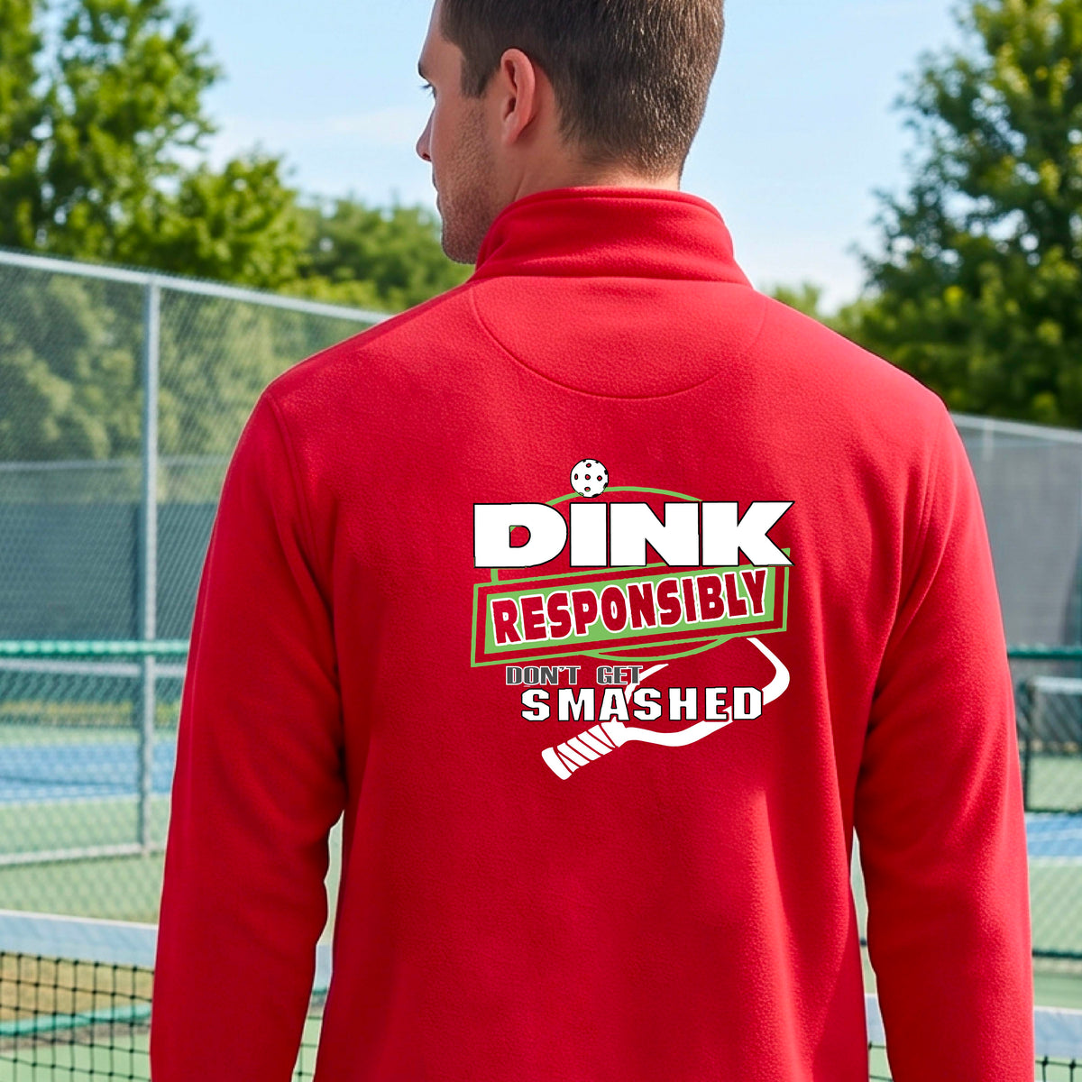 A man viewed from behind wearing a red long-sleeve athletic quarter-zip jacket with a large back graphic that reads 'DINK RESPONSIBLY DON'T LET SMASHED' with a white pickleball graphic on the design. 
