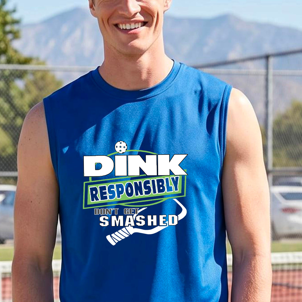 A man on a pickleball court wearing a royal blue sleeveless graphic shirt with the text 'DINK RESPONSIBLY DON'T GET SMASHED' in white and green, along with a white pickleball paddle under the text.