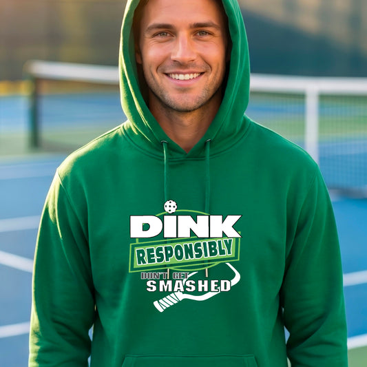 A man wearing a green hoodie with a white and green graphic that reads 'DINK RESPONSIBLY DON'T GET SMASHED' with a pickleball paddle icon, standing on a pickleball court. 