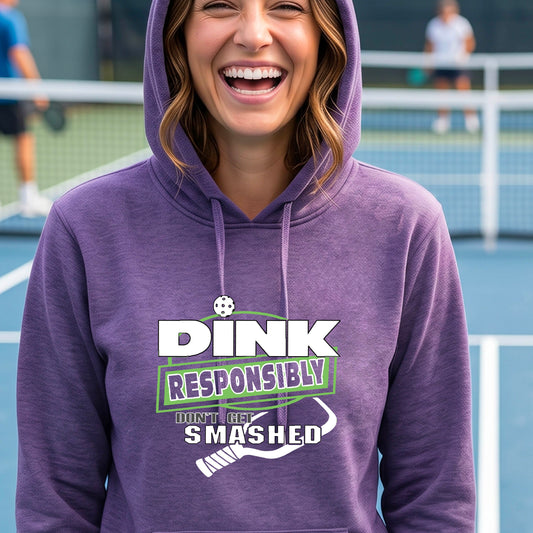 A woman wearing a purple graphic hoodie on a tennis court, with the text 'DINK RESPONSIBLY DON'T GET SMASHED' printed on the front with a white pickleball paddle graphic under the text. 