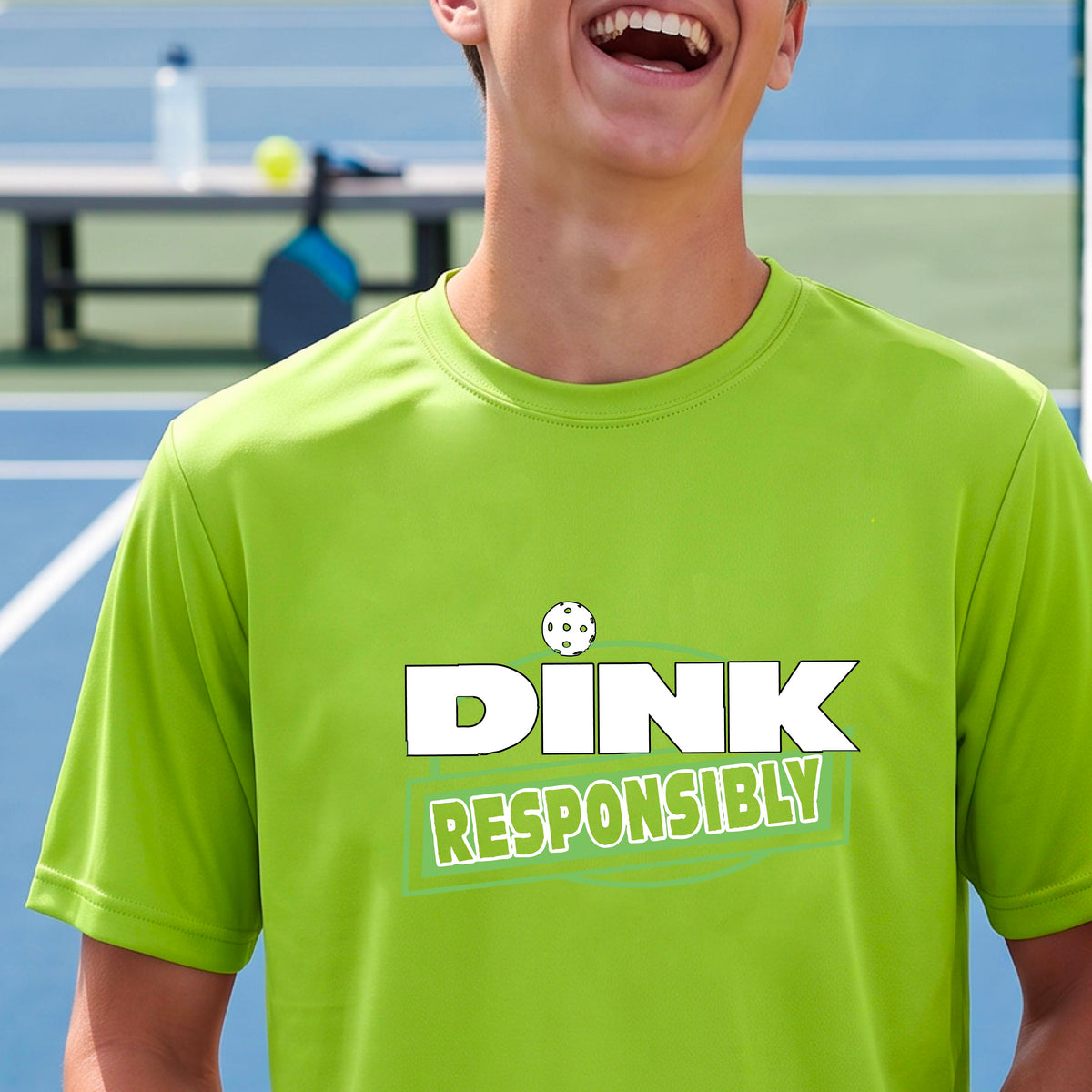 A smiling man wearing a lime green t-shirt with a green and white 'DINK RESPONSIBLY' graphic, standing on a pickleball court in the background.