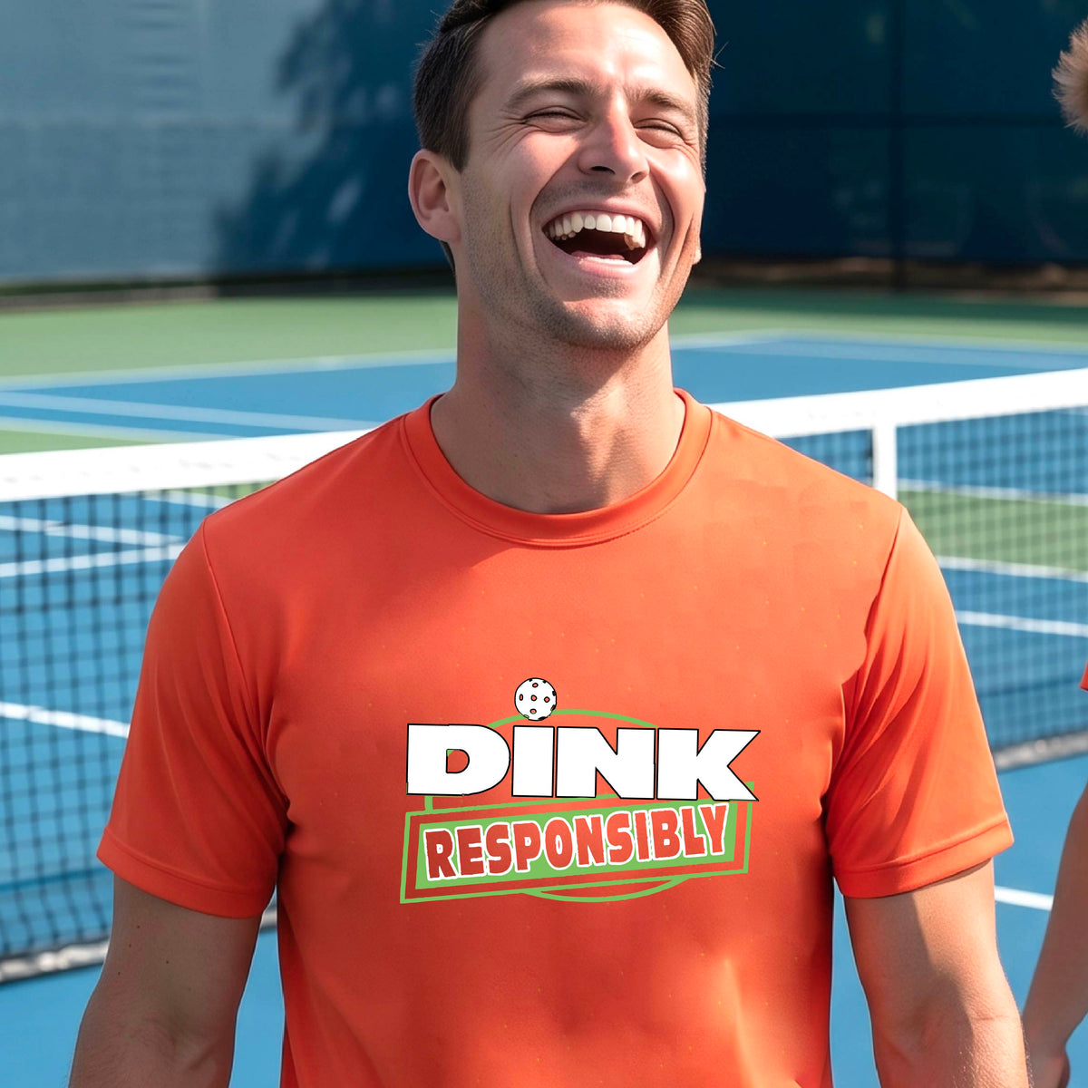 A smiling man wearing an orange t-shirt with a green and white 'DINK RESPONSIBLY' graphic, standing on a pickleball court in the background.