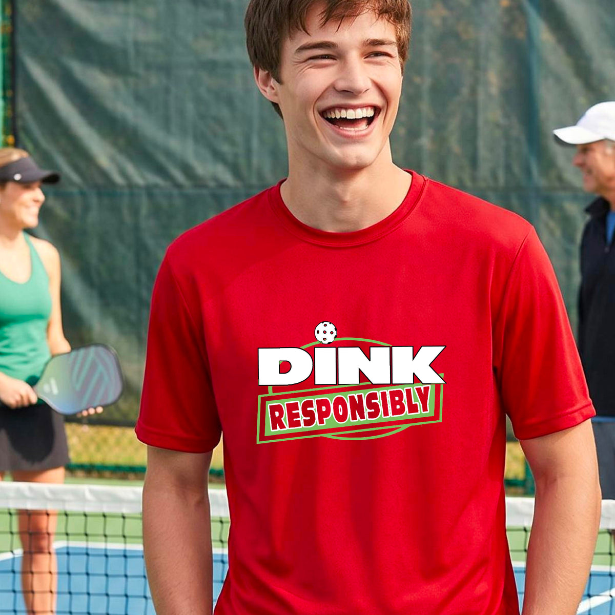 A smiling man wearing a red t-shirt with a green and white 'DINK RESPONSIBLY' graphic, standing on a pickleball court in the background.