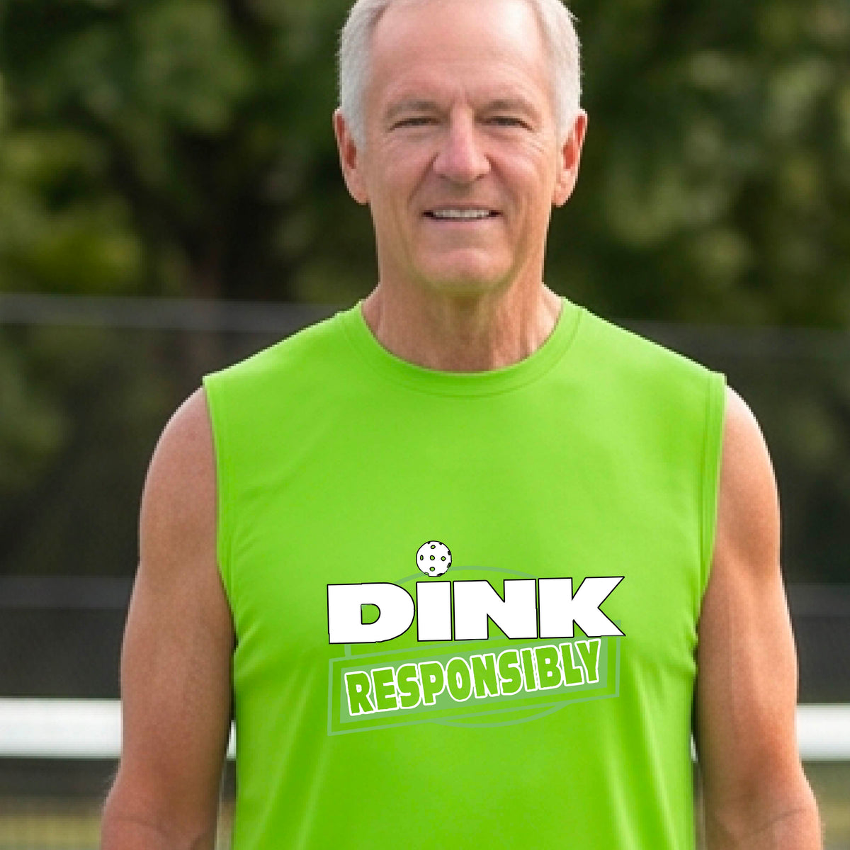 A smiling man wearing a lime green sleeveless athletic shirt with a green and white 'DINK RESPONSIBLY' graphic, standing on an outdoor pickleball court.