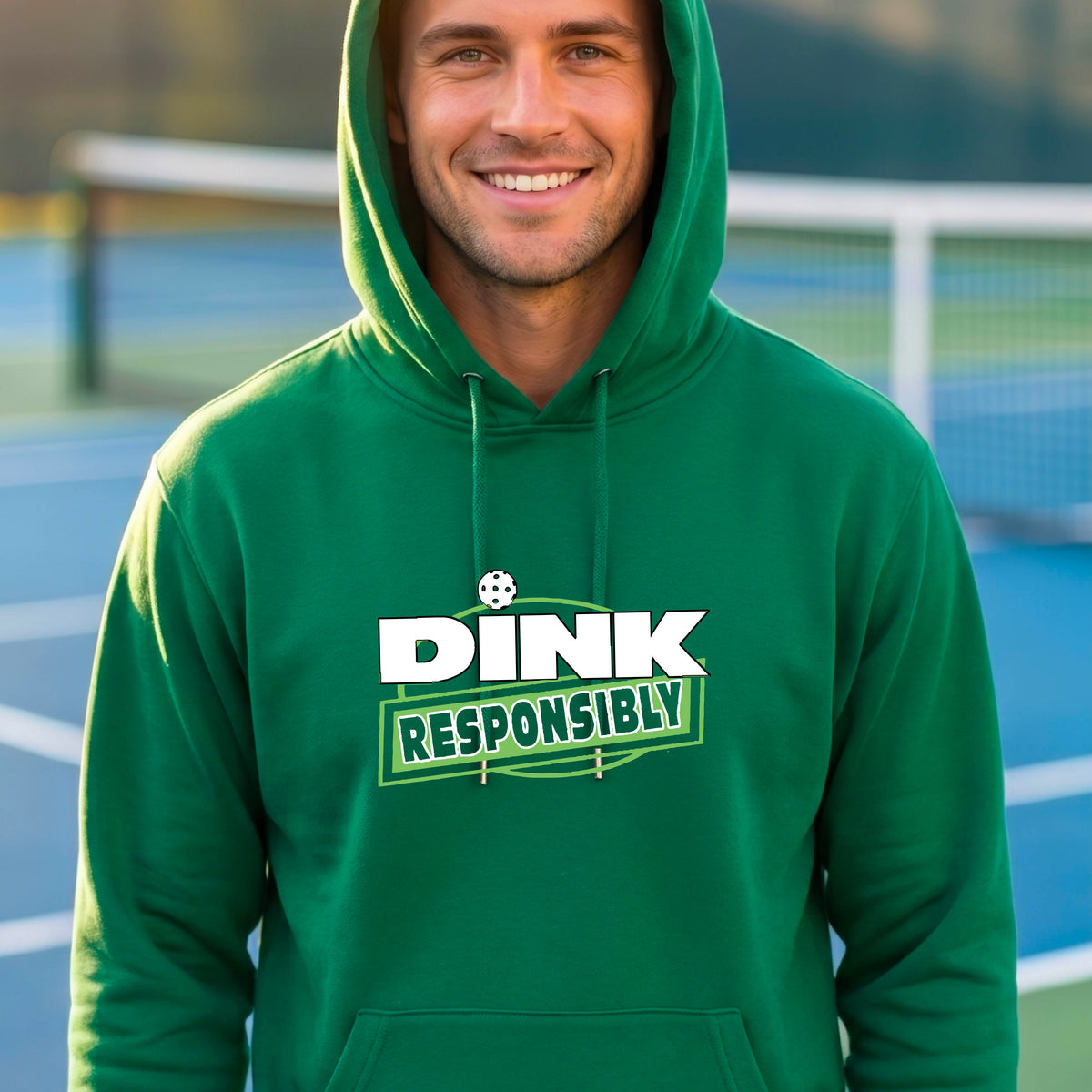 A man wearing a pickleball bright green pullover hoodie with a graphic on the chest that reads 'DINK RESPONSIBLY' in white and green on a pickleball court. 