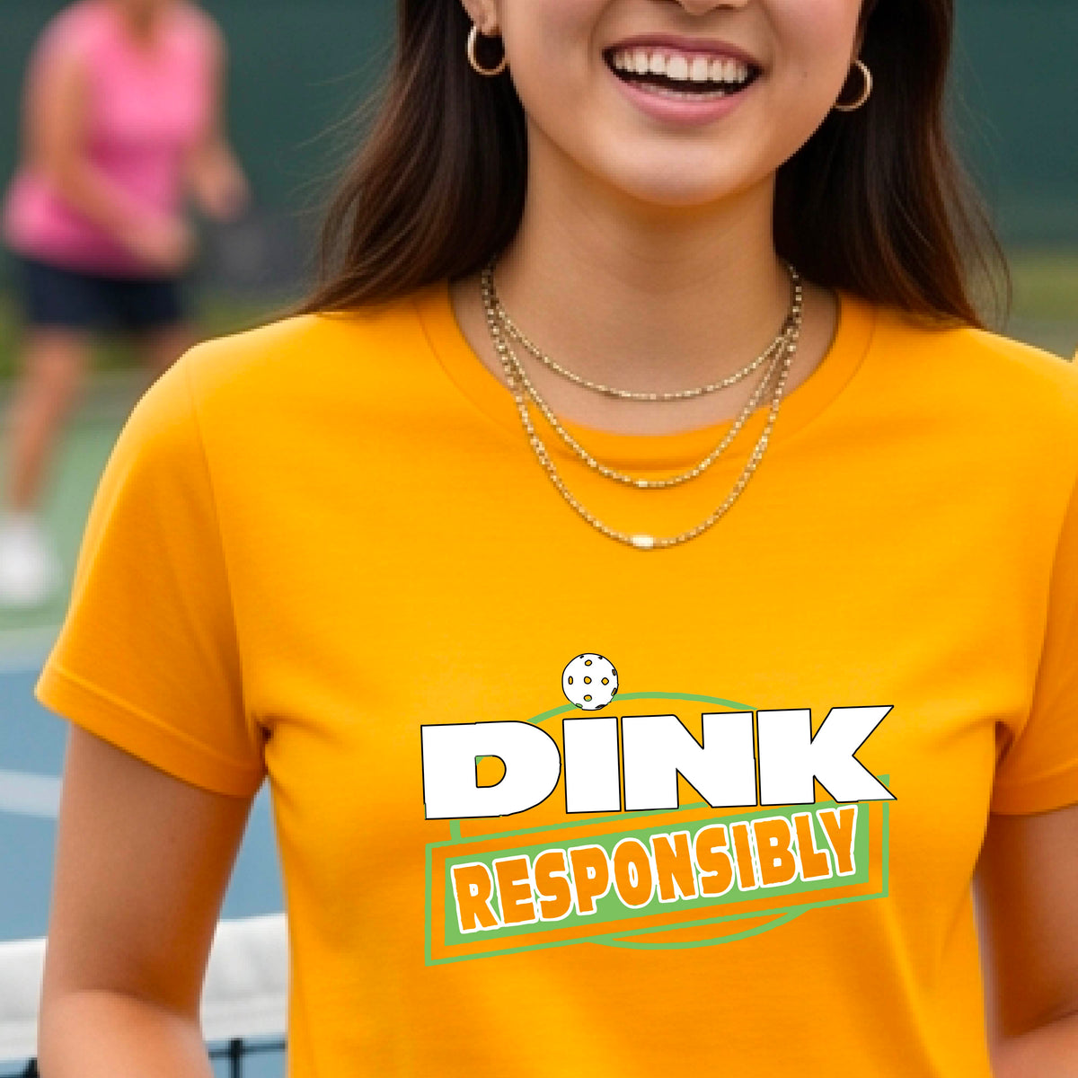 A woman wearing a pickleball mustard yellow gold short-sleeve graphic t-shirt with the text 'DINK RESPONSIBLY' in white and green.