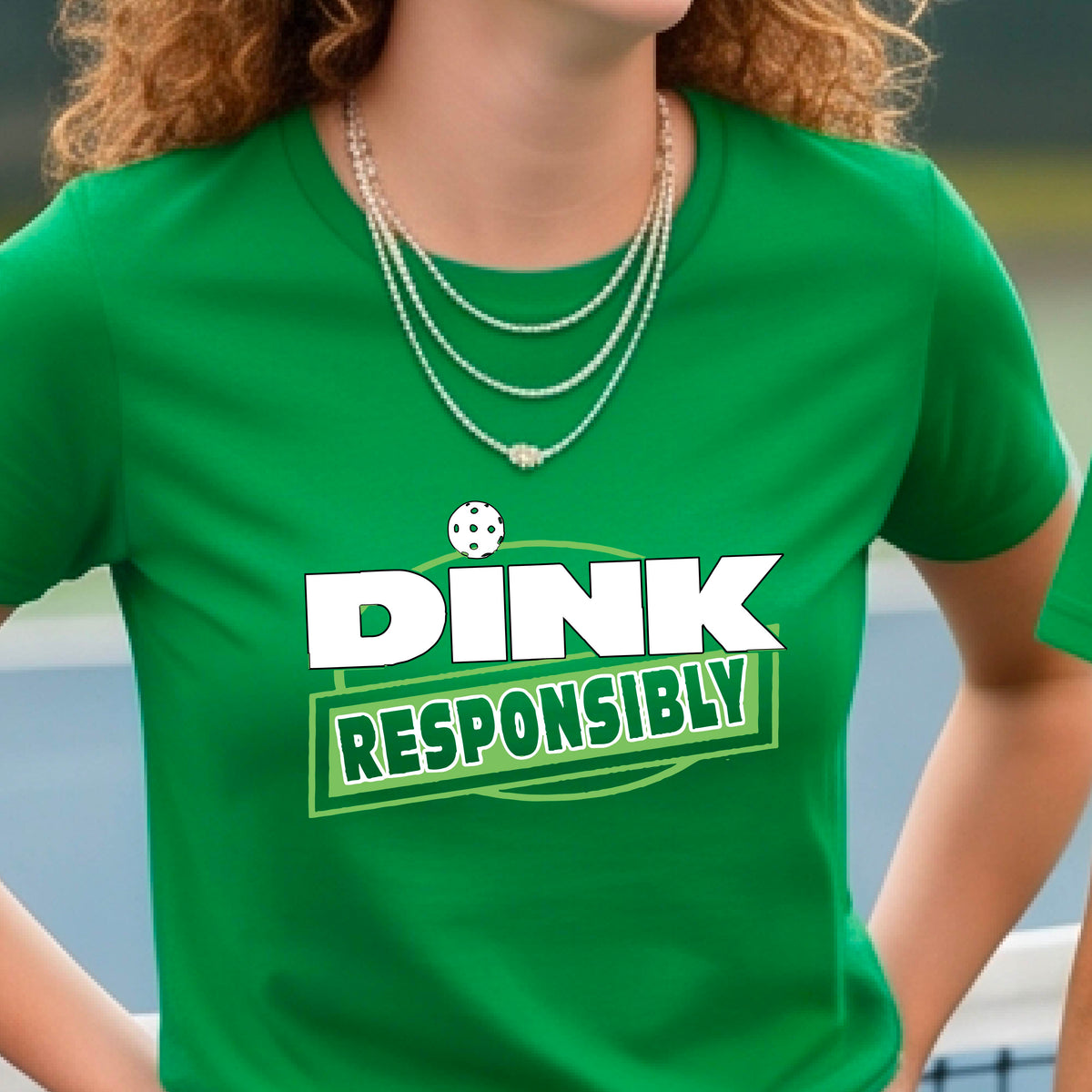 A woman wearing a pickleball green short-sleeve graphic t-shirt with the text 'DINK RESPONSIBLY' in white and green.