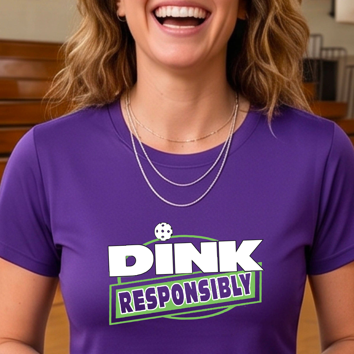 A woman wearing a pickleball purple short-sleeve graphic t-shirt with the text 'DINK RESPONSIBLY' in white and green.