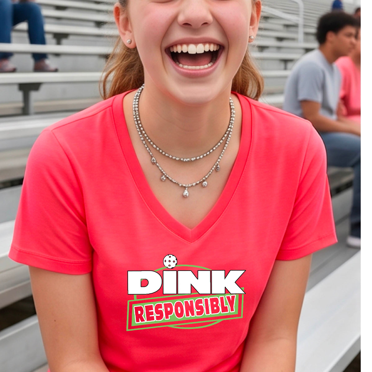 A woman wearing a coral pink V-neck t-shirt with a pickleball 'DINK RESPONSIBLY' graphic on the ches.