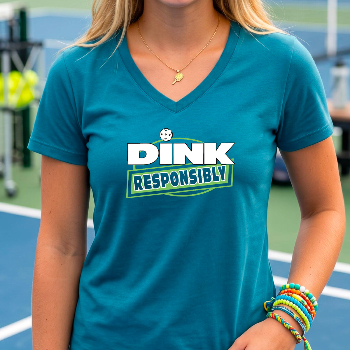 A woman wearing a teal V-neck t-shirt with a pickleball 'DINK RESPONSIBLY' graphic on the ches.