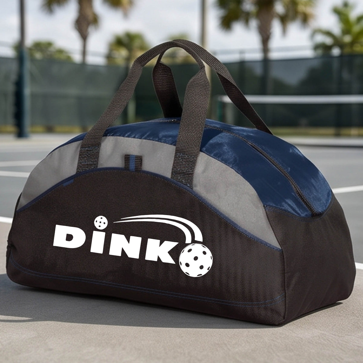 A close up of a navy blue, black and gray pickleball  duffel bag with a pickleball design of text 'DINK' with a white pickleall in flight, on a pickleball court .