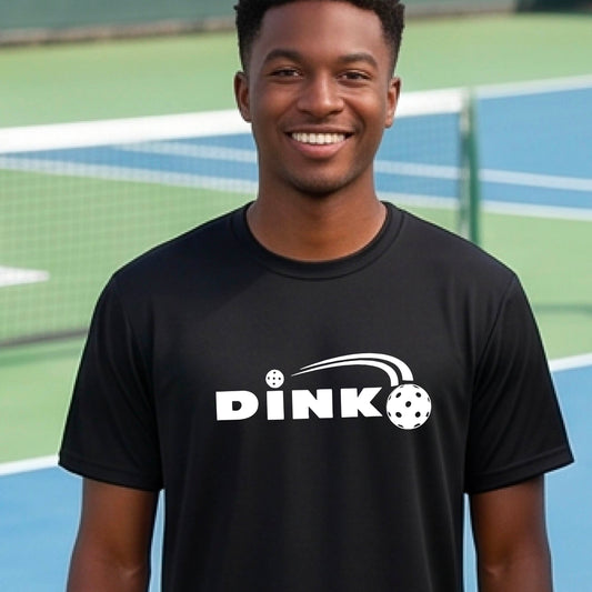 A man wearing a black short-sleeve t-shirt with a pickleball design of text 'DINK' with a white pickleall in flight, standing on a pickleball court.