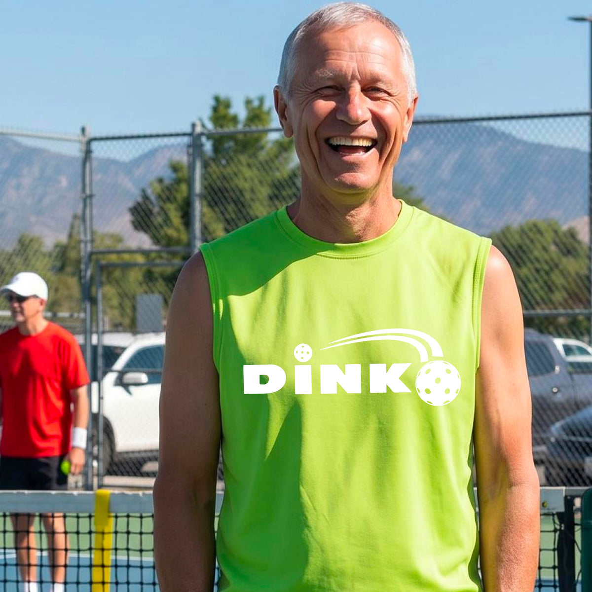 A man wearing a lime green sleeveless t-shirt with a pickleball design of text 'DINK' with a white pickleall in flight, standing on a pickleball court.
