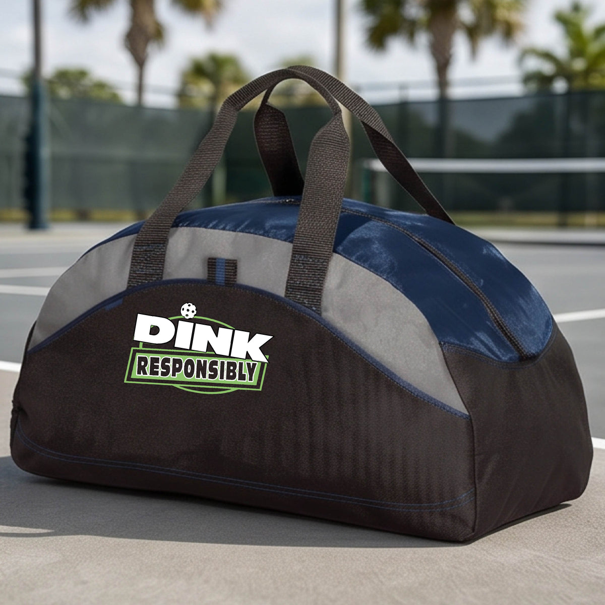 A navy blue, black, and gray duffel bag with custom 'DINK RESPONSIBLY' branding, placed on a pickleball court with a blue court visible in the background.