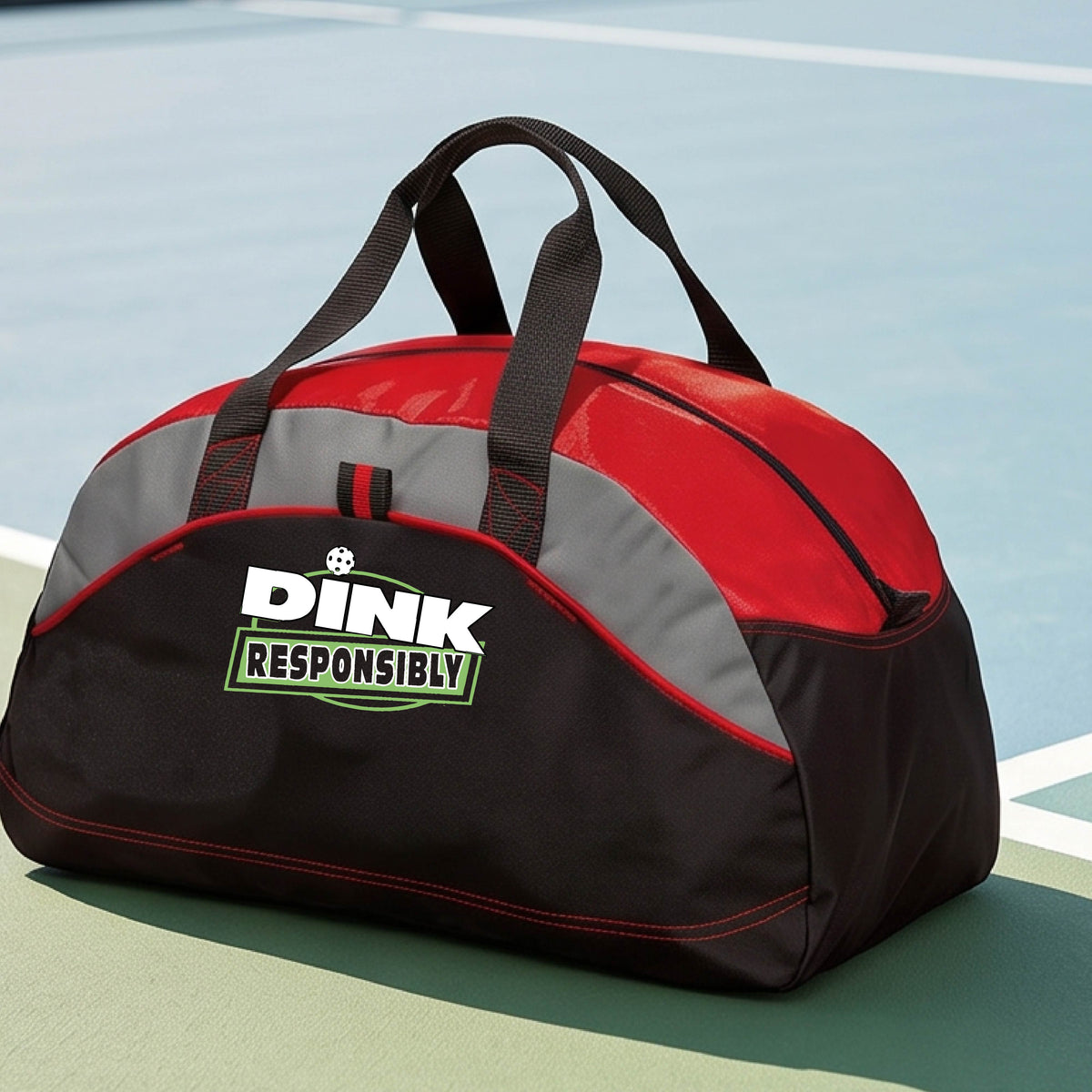 A red, black, and gray duffel bag with custom 'DINK RESPONSIBLY' branding, placed on a pickleball court with a blue court visible in the background.
