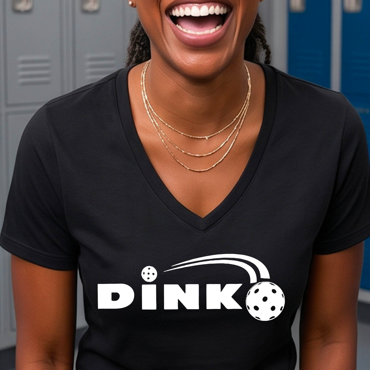 A woman wearing a black short-sleeve v-neck t-shirt with a pickleball design of text 'DINK' with a white pickleall in flight, standing on a pickleball court.