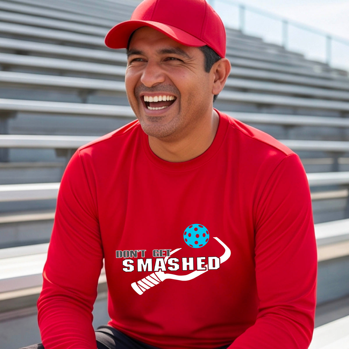 A man wearing a red long-sleeve t-shirt with a white graphic with the text 'DON'T GET SMASHED' and a white pickleball paddle and colorful pickleall graphic.