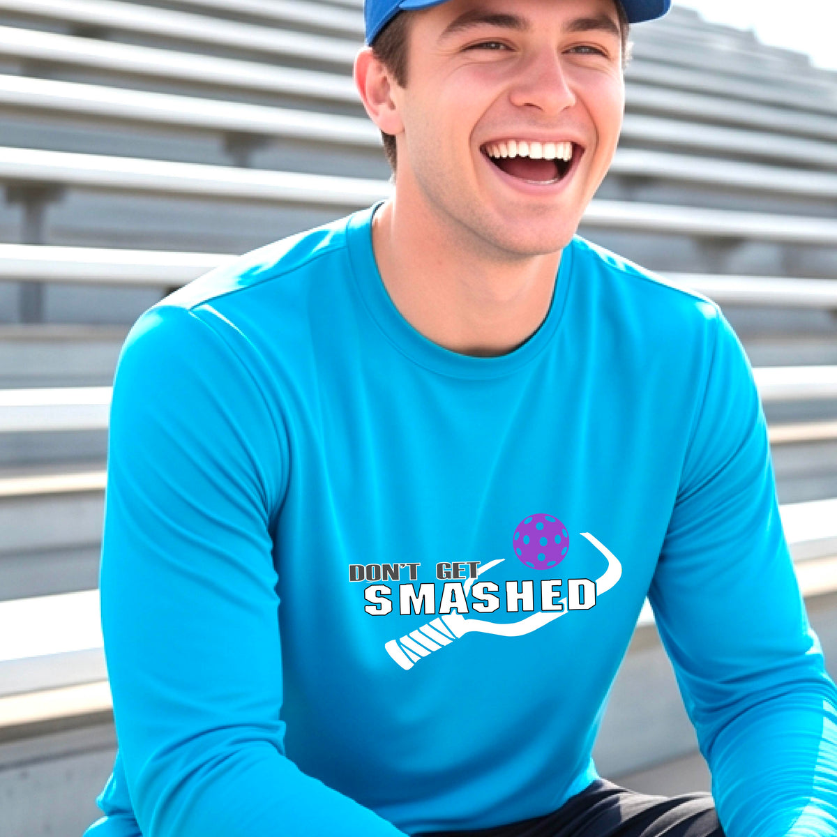 A man wearing a bright blue long-sleeve t-shirt with a white graphic with the text 'DON'T GET SMASHED' and a white pickleball paddle and colorful pickleall graphic. 