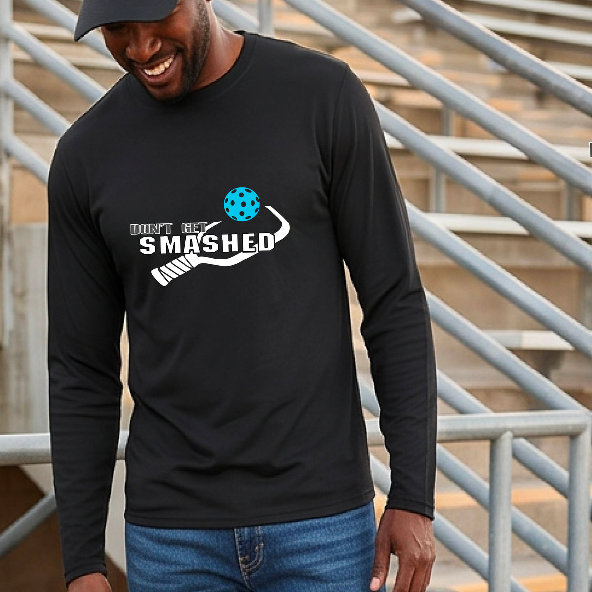 A man wearing a black long-sleeve t-shirt with a white graphic with the text 'DON'T GET SMASHED' and a white pickleball paddle and colorful pickleall graphic. 