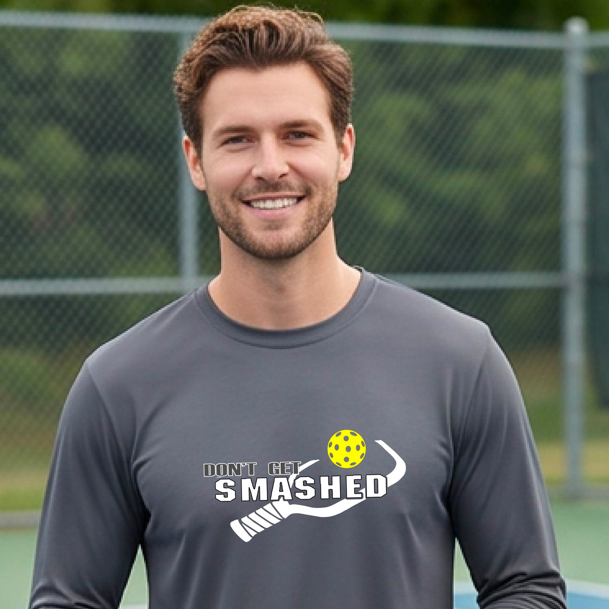 A man wearing a gray long-sleeve t-shirt with a white graphic with the text 'DON'T GET SMASHED' and a white pickleball paddle and colorful pickleall graphic. 
