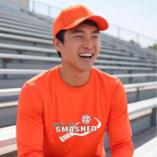 A man wearing an orange long-sleeve t-shirt with a white graphic with the text 'DON'T GET SMASHED' and a white pickleball paddle and colorful pickleall graphic. 