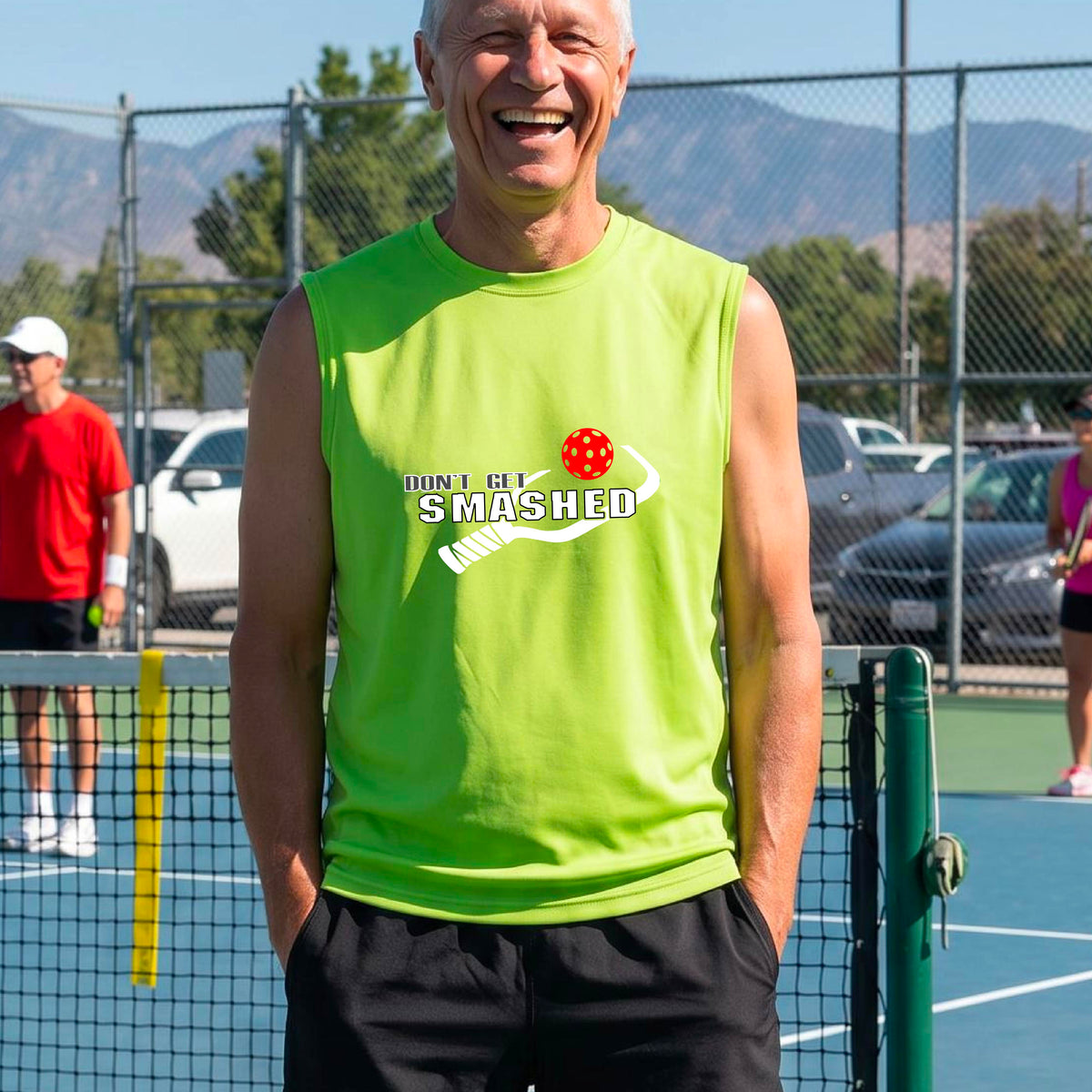 A smiling man wearing a lime green sleeveless t-shirt with a yellow and white graphic that reads 'DON'T GET SMASHED' with a white pickleball paddle and colorful pickleball graphic.