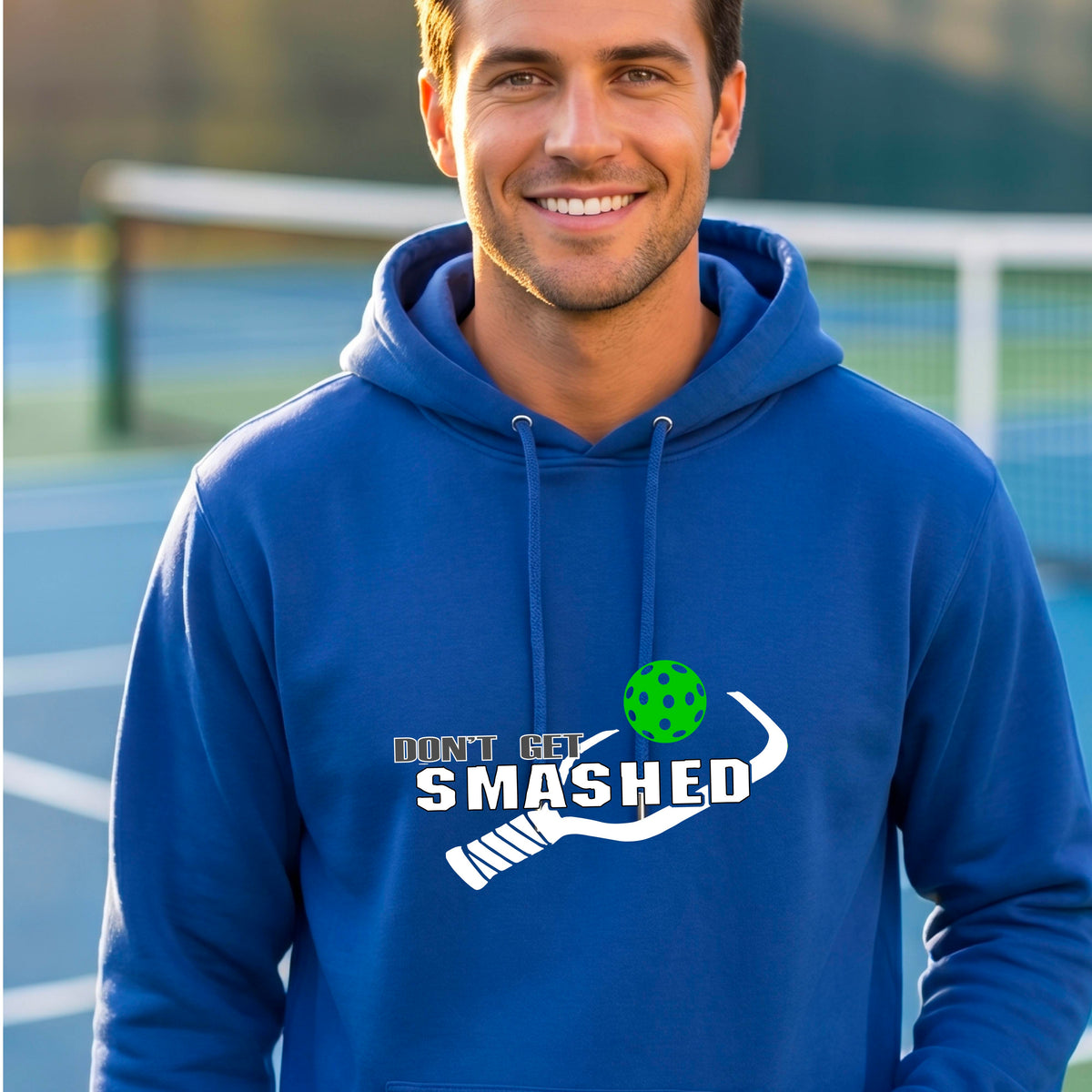 A man wearing a royal blue pullover hoodie with a white graphic print on the chest that reads 'DON'T GET SMASHED' with a pickleball paddle and colorful pickleball design.