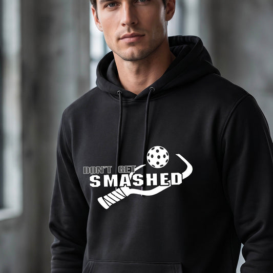 A man wearing a black pullover hoodie with a white graphic print on the chest that reads 'DON'T GET SMASHED' with a pickleball paddle and colorful pickleball design.