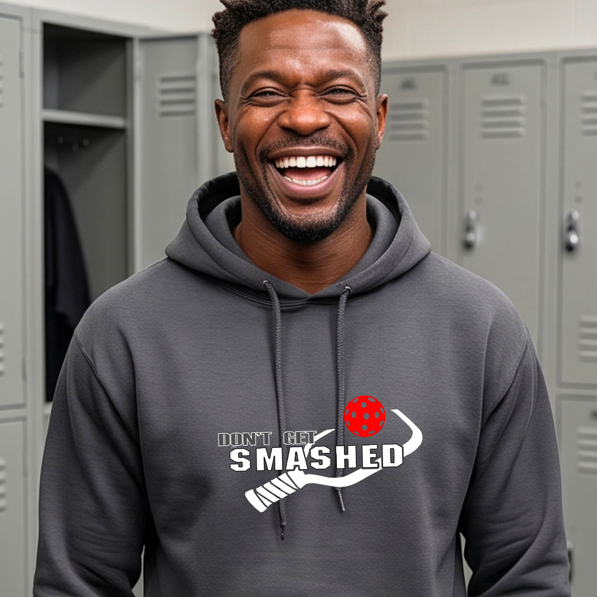 A man wearing a gray pullover hoodie with a white graphic print on the chest that reads 'DON'T GET SMASHED' with a pickleball paddle and colorful pickleball design.