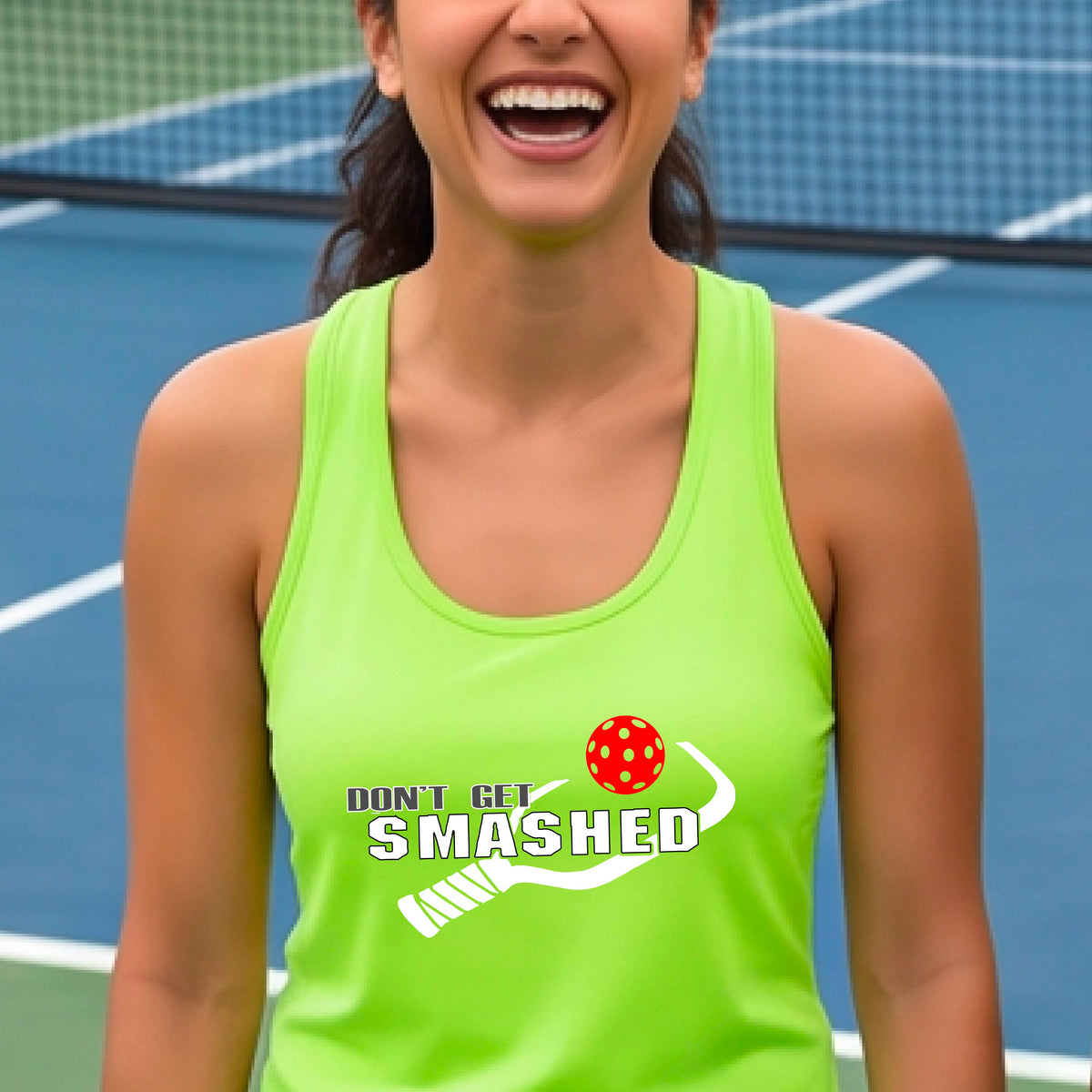 A woman on a pickleball court wearing a lime green athletic racerback tank top with a white and green 'DON'T GET SMASHED' graphic with a pickleball paddle and colorful pickleball. 
