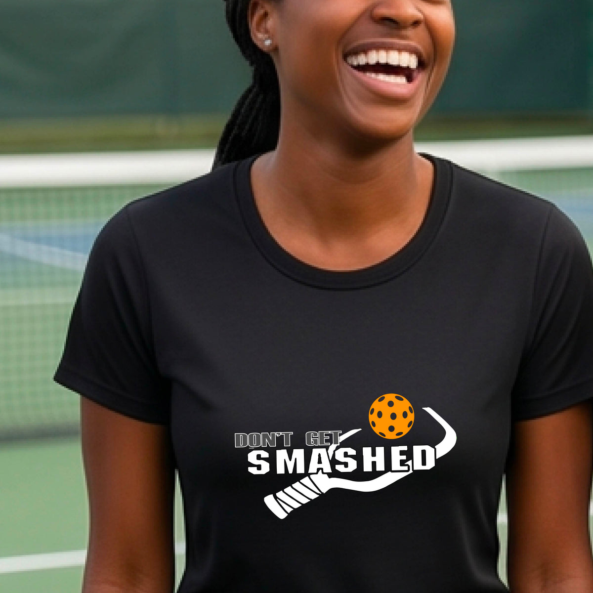 A close-up of a woman wearing a black t-shirt with a graphic that reads 'DON'T GET SMASHED' in white accompanied by a colorful pickleball and a white pickleball paddle.
