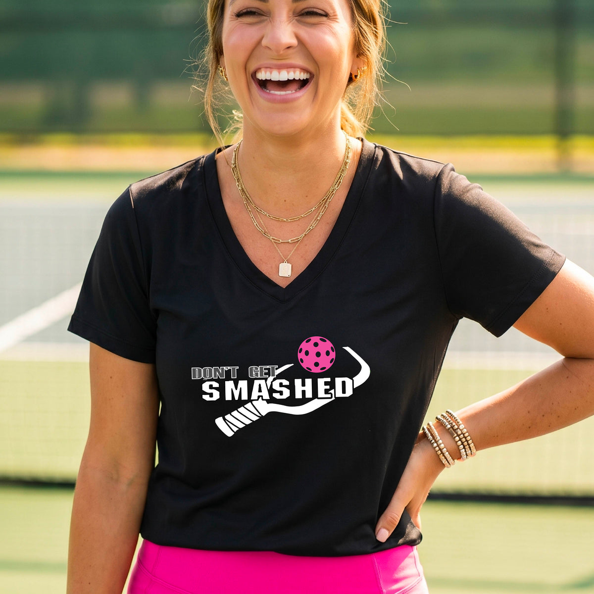 A woman wearing a black V-neck t-shirt with a white graphic that reads 'DON'T GET SMASHED' alongside a pickleball paddle and a colorful pickleball.