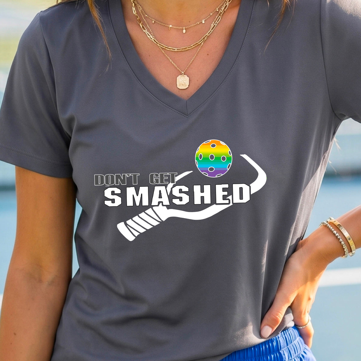 A woman wearing a gray V-neck t-shirt with a white graphic that reads 'DON'T GET SMASHED' alongside a pickleball paddle and a colorful pickleball.