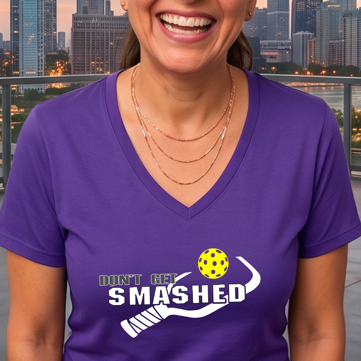 A woman wearing a purple V-neck t-shirt with a white graphic that reads 'DON'T GET SMASHED' alongside a pickleball paddle and a colorful pickleball.