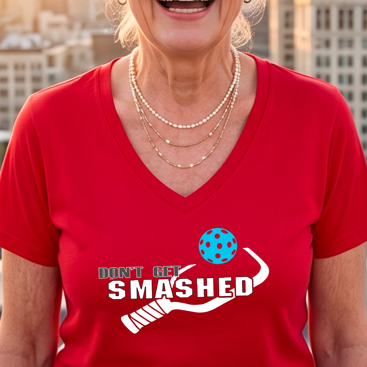 A woman wearing a red V-neck t-shirt with a white graphic that reads 'DON'T GET SMASHED' alongside a pickleball paddle and a colorful pickleball.