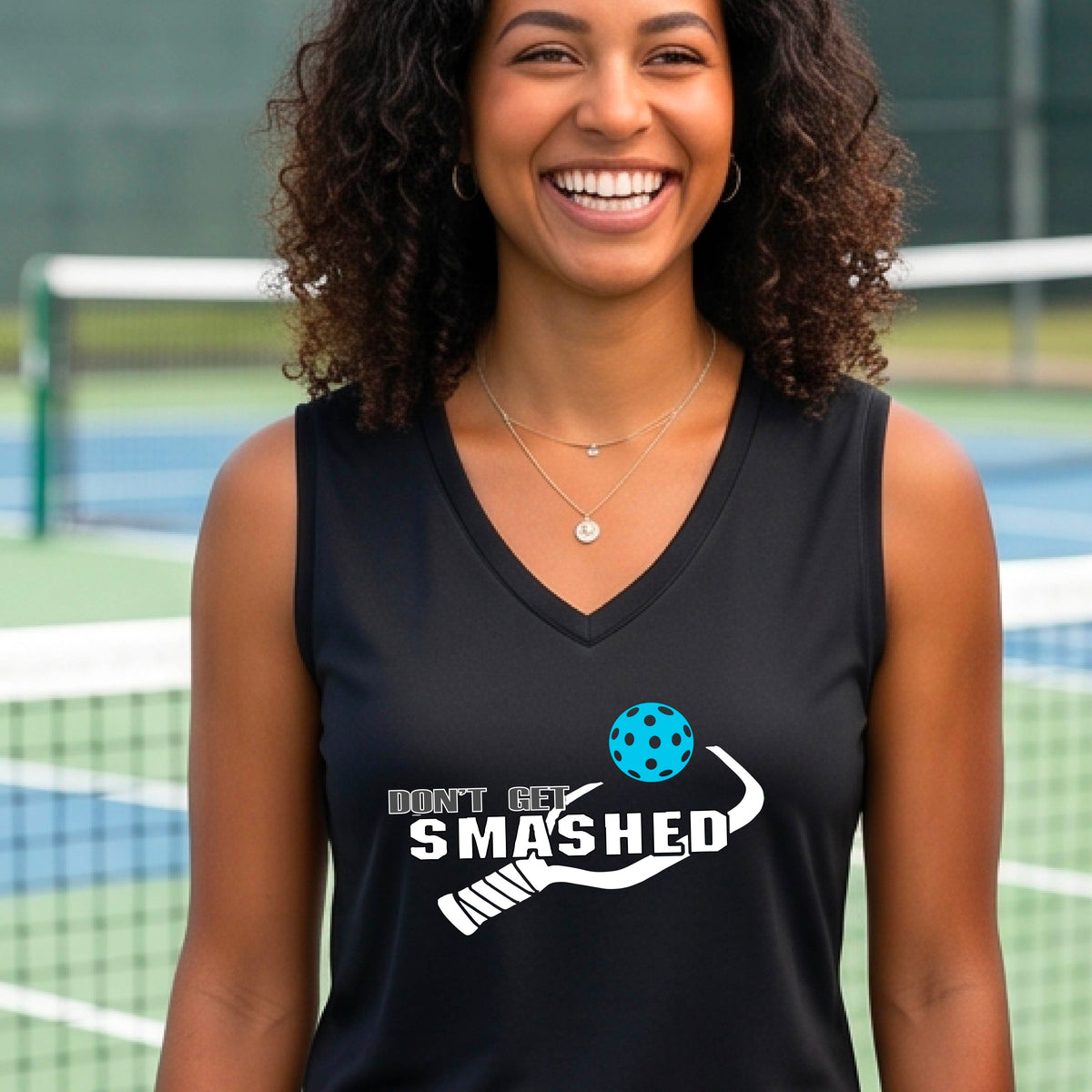 A smiling woman wearing a black sleeveless V-neck athletic tank top with a pickleball -themed graphic that reads 'DON'T GET SMASHED' and shows a white pickleball paddle and colorful pickleball. 