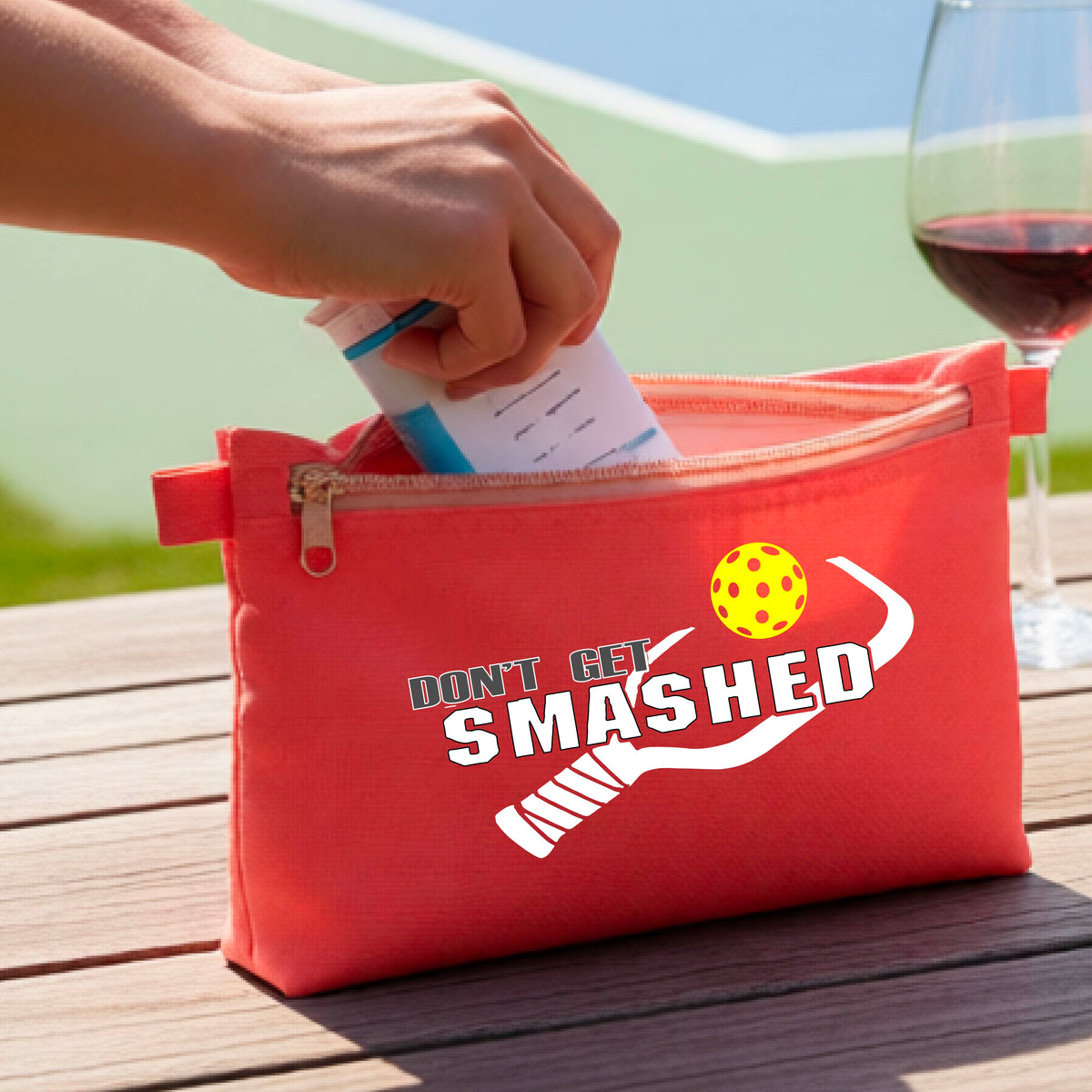 A coral colored cosmetic toiletry pouch with a white 'DON'T GET SMASHED' graphic including a pickleball paddle and a colorful pickleball graphic. 