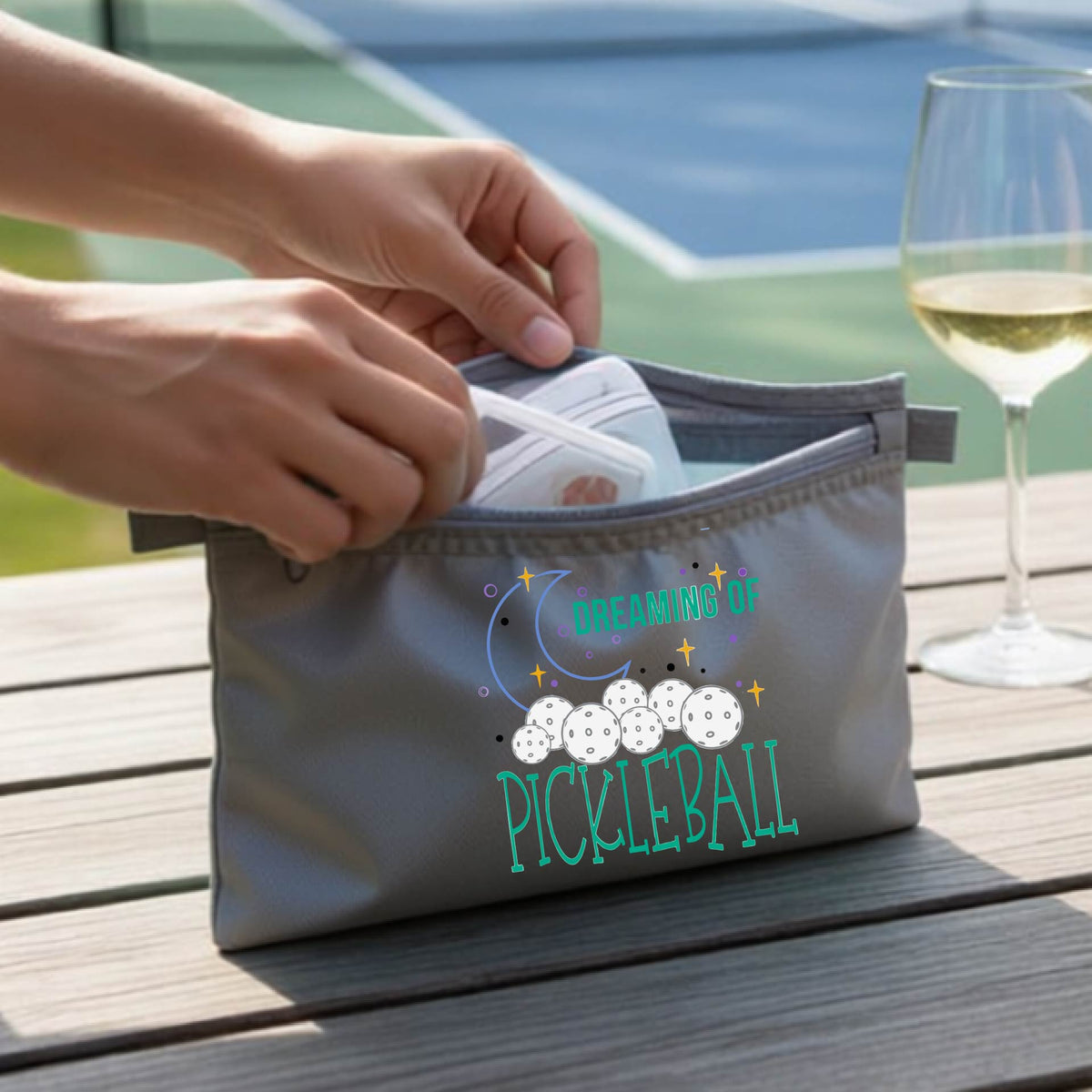 A gray zippered pickleball pouch with a printed graphic of pickleballs, a crescent moon, and the words 'DREAMING OF PICKLEBALL.