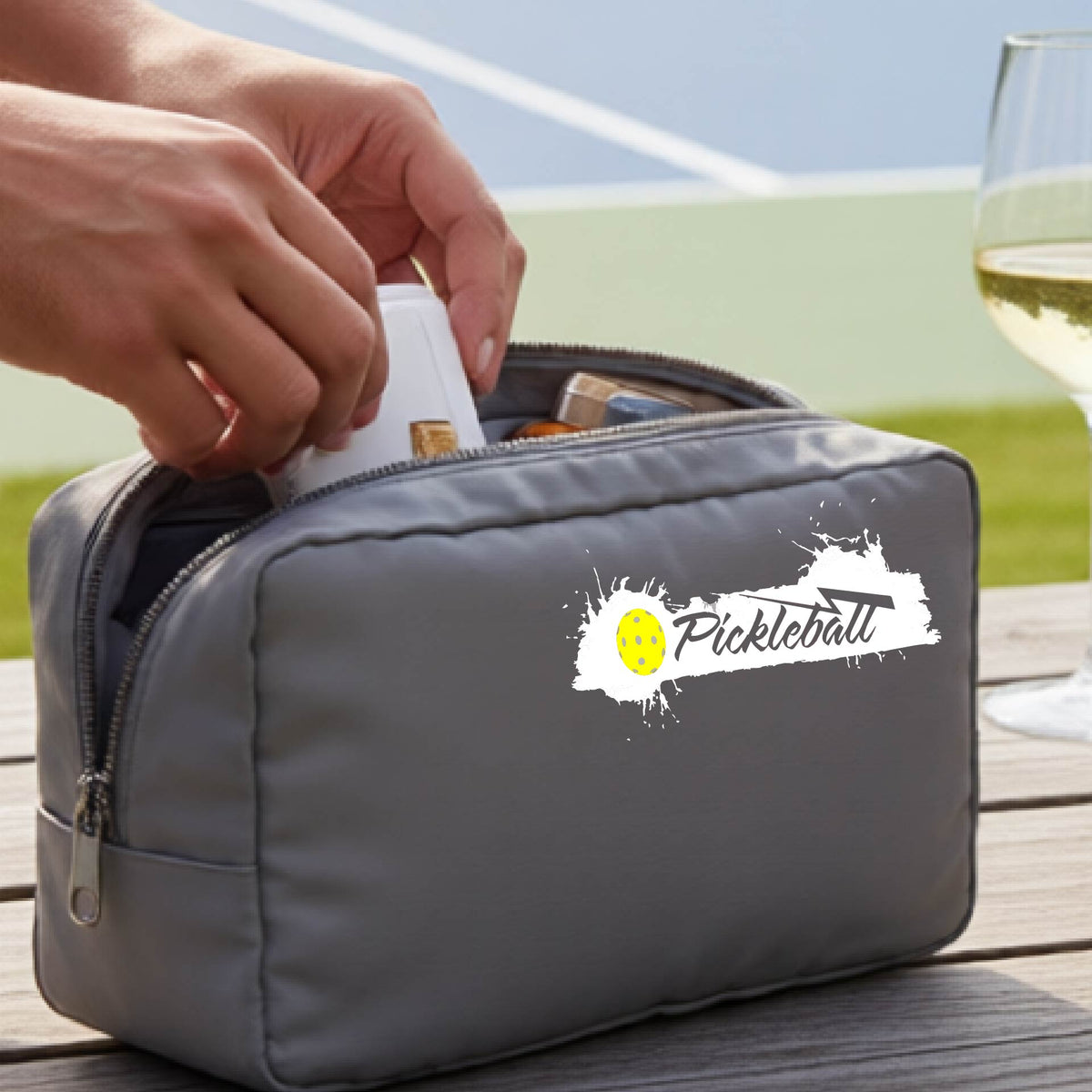 A gray zippered pickleball-themed cosmetic bag with a white pickleball splaltter graphic and pickleball icon. 