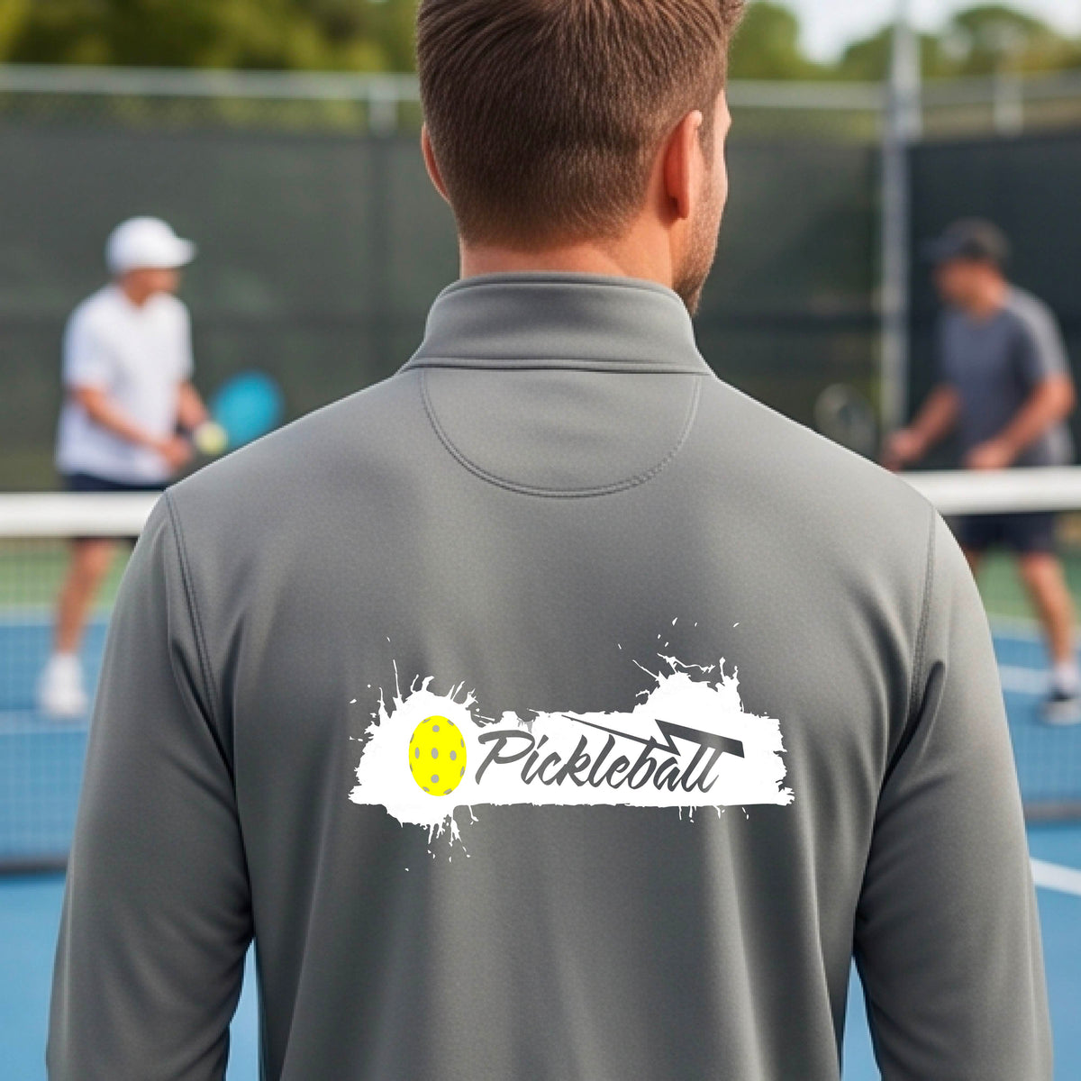 A man viewed from behind wearing a gray long-sleeve quarter-zip athletic shirt with a 'Pickleball' splatter  graphic standing on a pickleball court. 