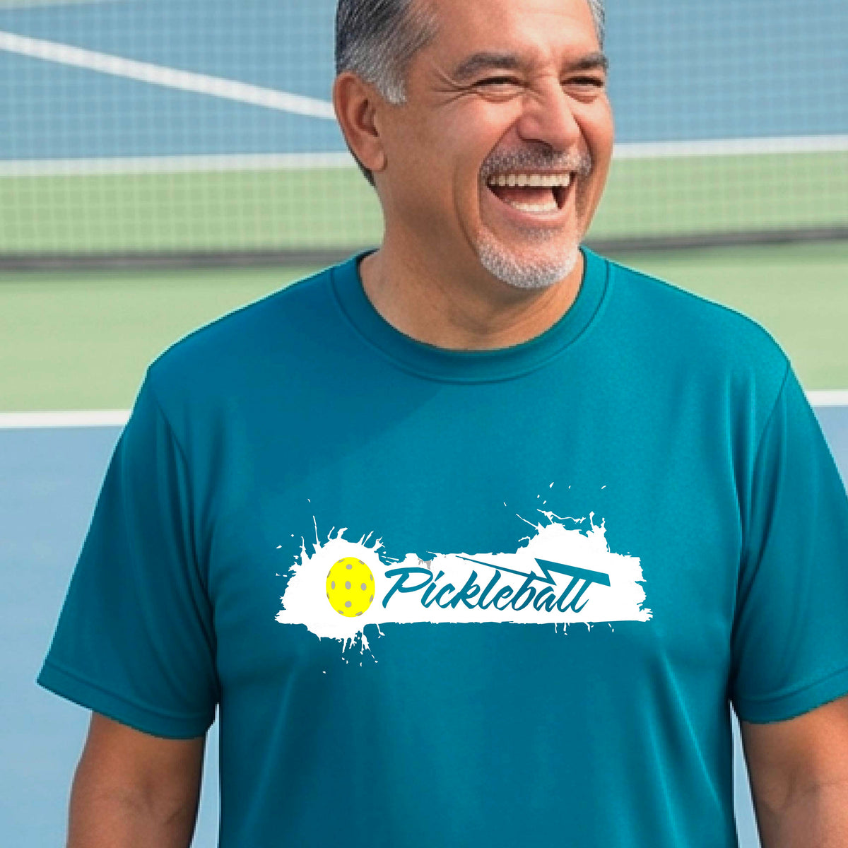 A smiling man wearing a teal t-shirt with a 'Pickleball' splatter graphic on the chest, 
