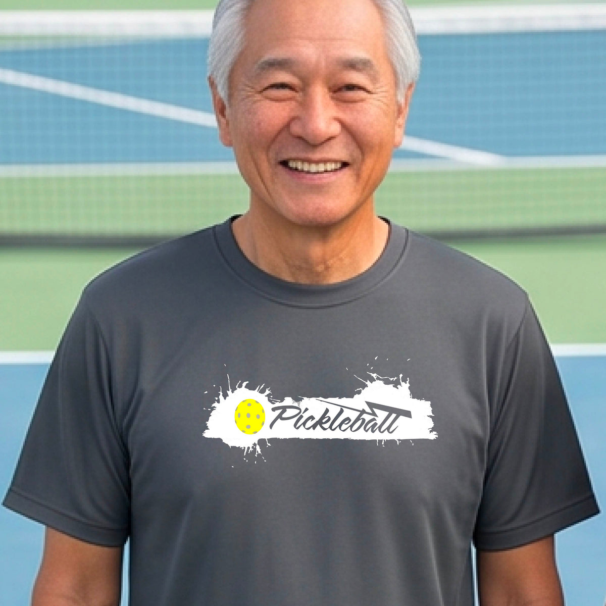 A smiling man wearing a gray t-shirt with a 'Pickleball' splatter graphic on the chest, 