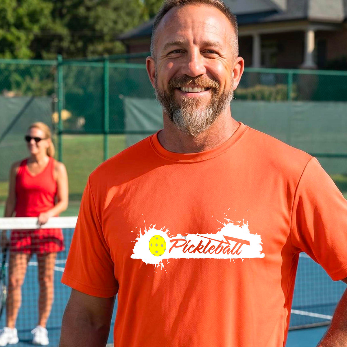 A smiling man wearing an orange t-shirt with a 'Pickleball' splatter graphic on the chest, 