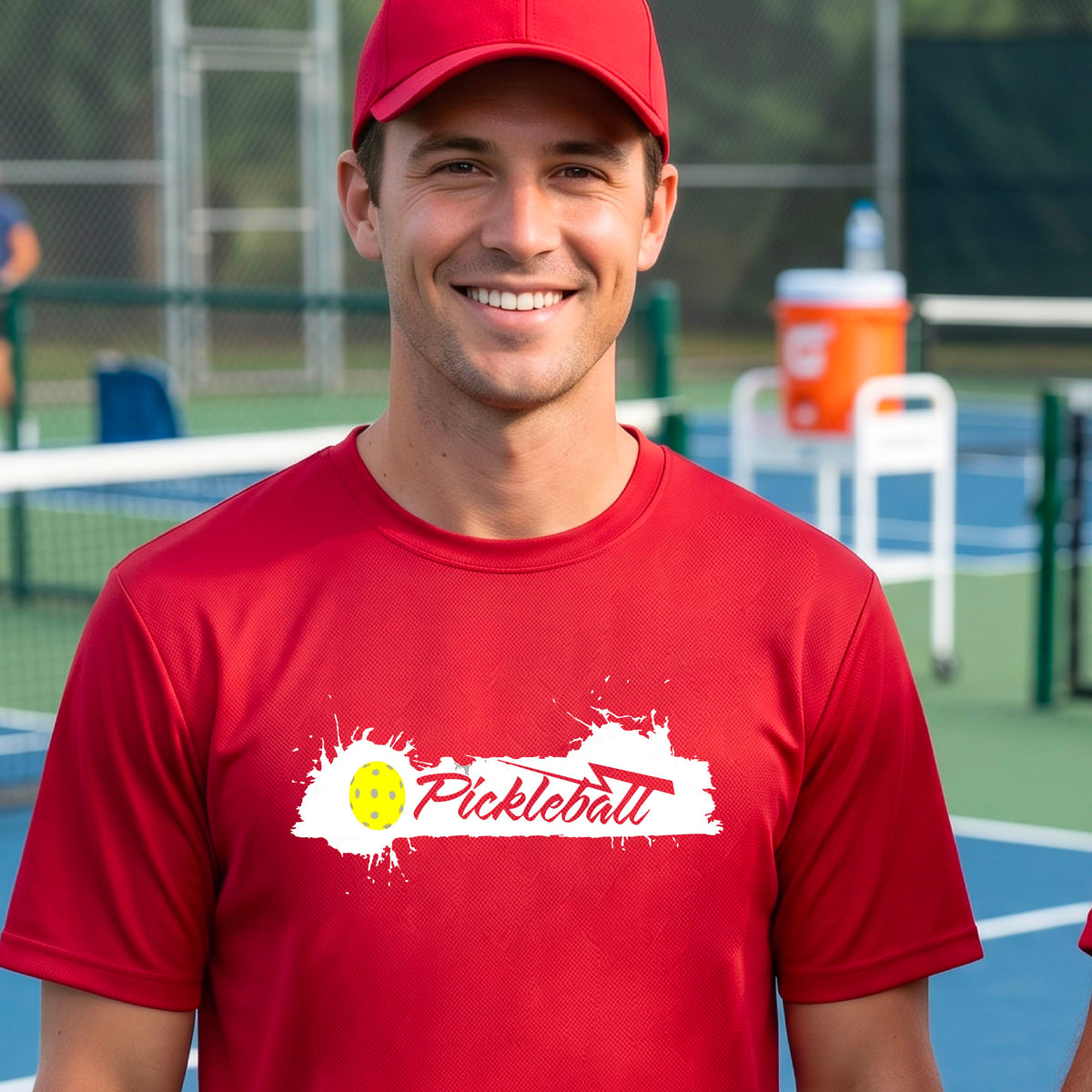 A smiling man wearing a red t-shirt with a 'Pickleball' splatter graphic on the chest, 