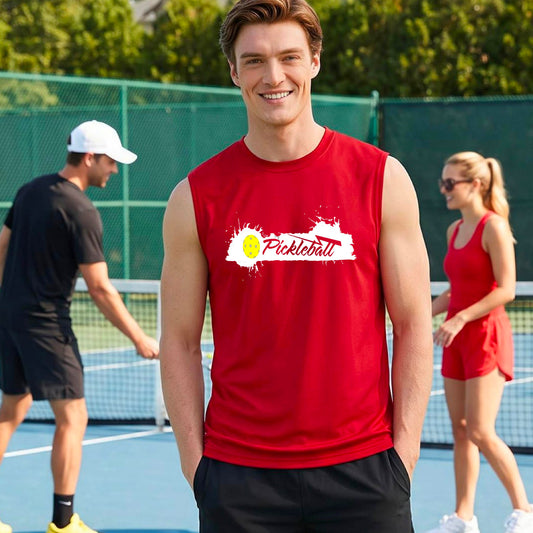 A smiling man wearing a red sleeveless athletic tank top with a 'Pickleball' splatter graphic stands on an outdoor pickleball court. 