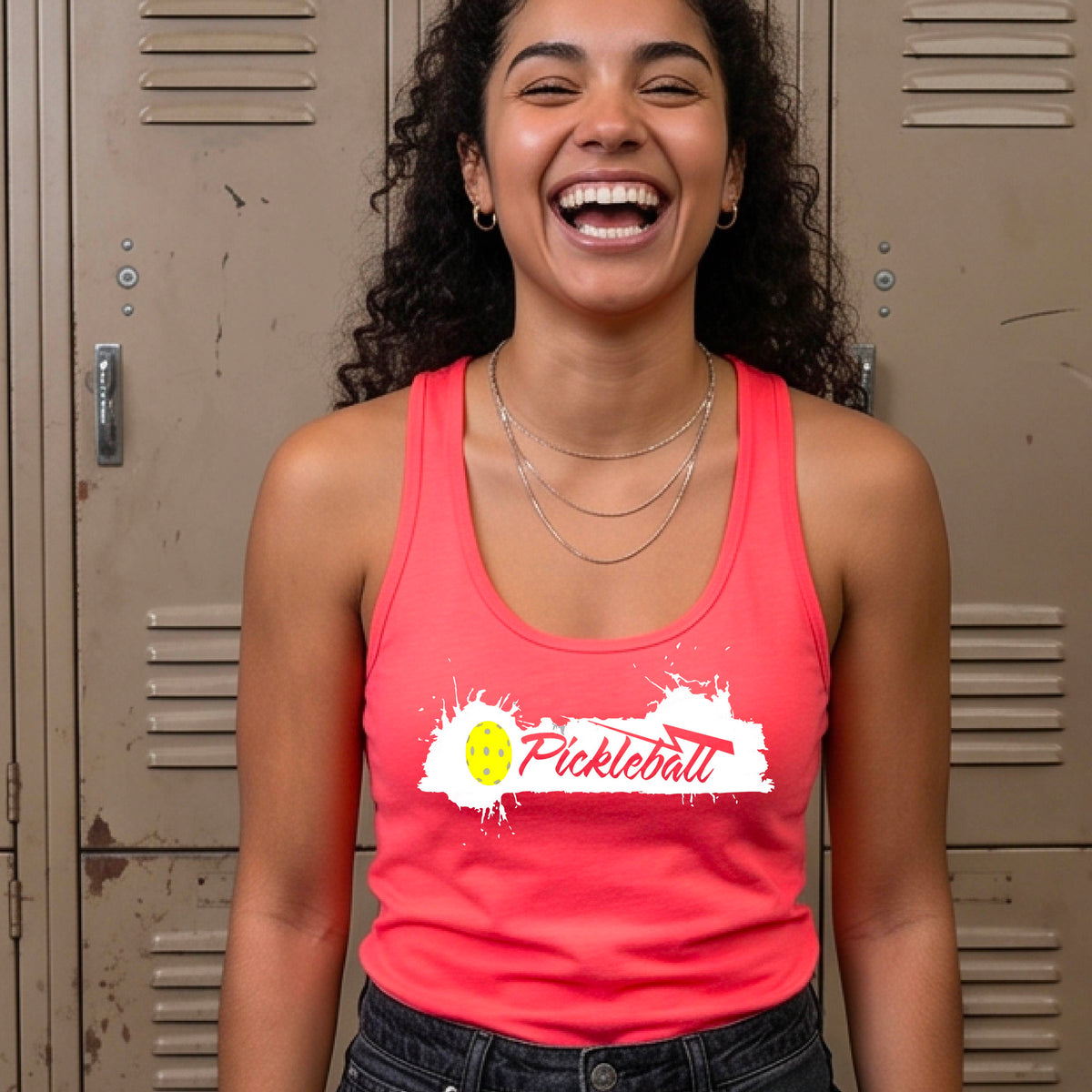 A smiling woman wearing a coral pink racerback athletic tank top with a white and yellow 'Pickleball' graphic on the front.