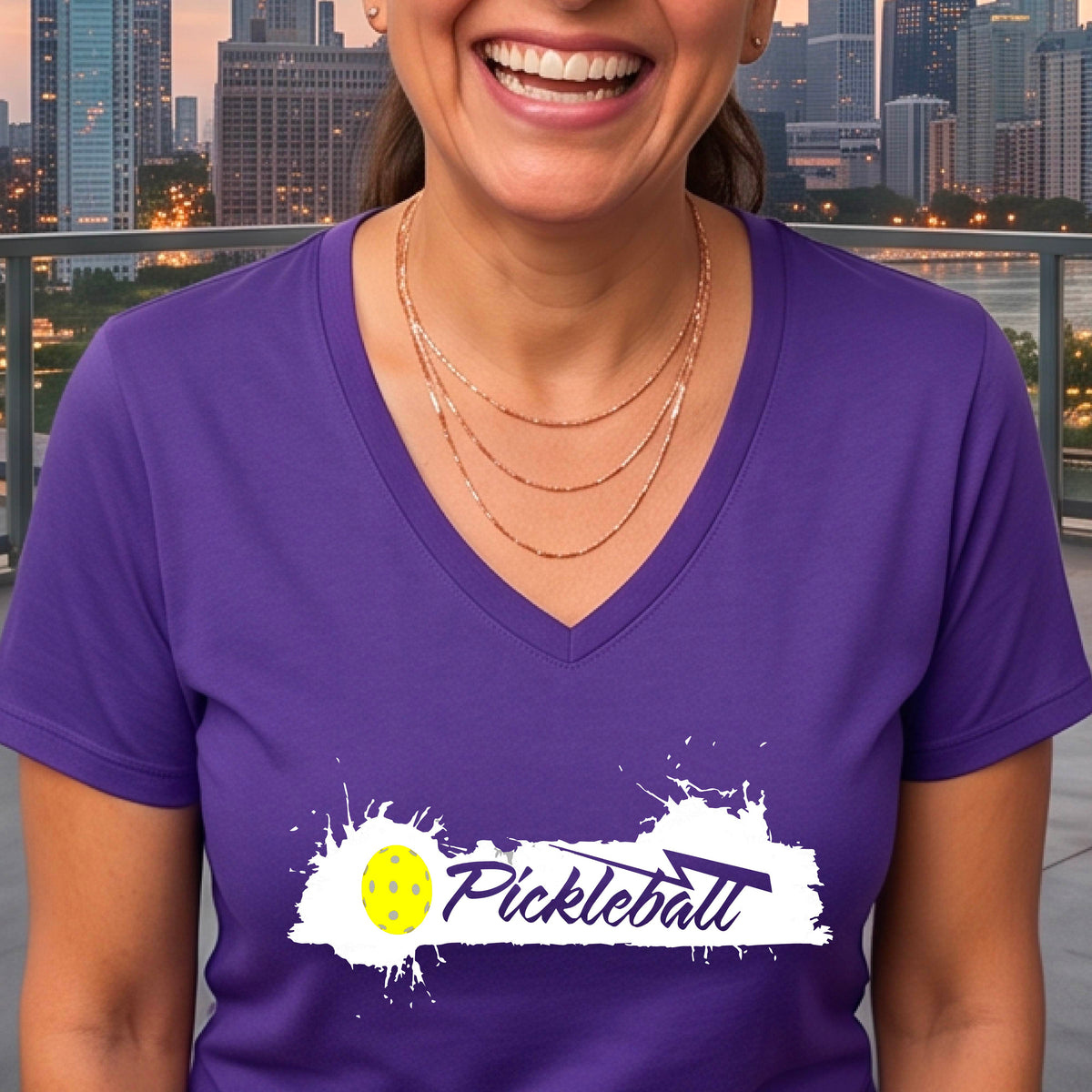 A woman wearing a purple V-neck t-shirt with a white and yellow 'Pickleball' splatter graphic on the front..