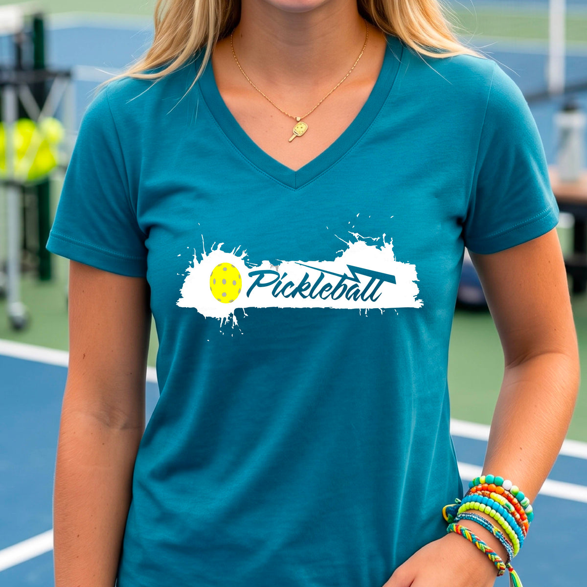 A woman wearing a teal V-neck t-shirt with a white and yellow 'Pickleball' splatter graphic on the front..
